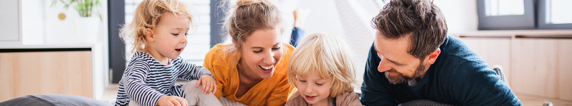 Young family with two small children indoors in bedroom reading a book.