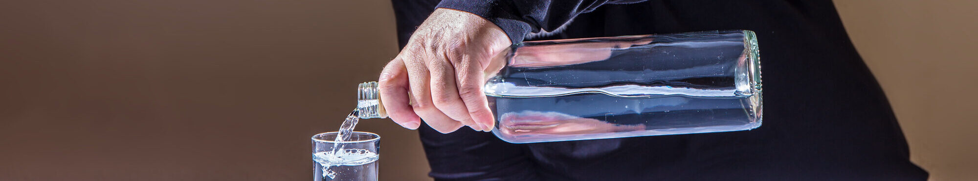 An elderly man sits at a table and pours alcohol into a glass