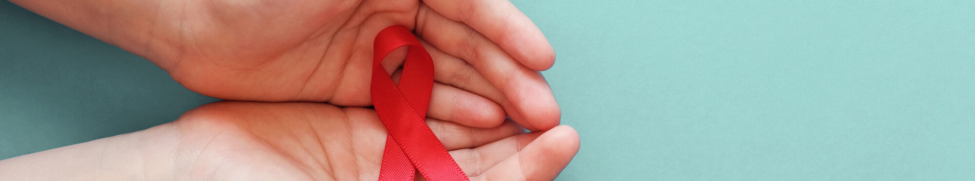 Hands holding red ribbon on blue background, hiv awareness concept, world AIDS day, world hypertension day