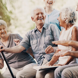 Happy elderly man with walking stick and smiling senior people relaxing in the garden